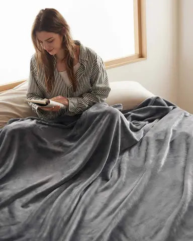Woman reading while relaxing under a soft gray fleece blanket on a cozy bed