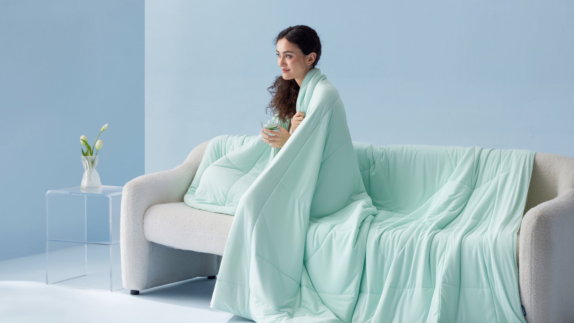 Woman wrapped in a lightweight cooling comforter on a sofa