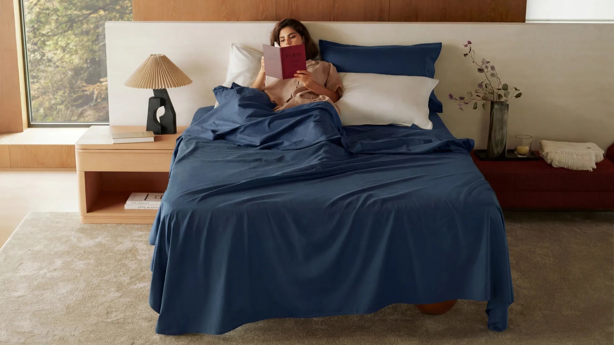 Woman reading a book in bed with dark blue sheets and white pillows