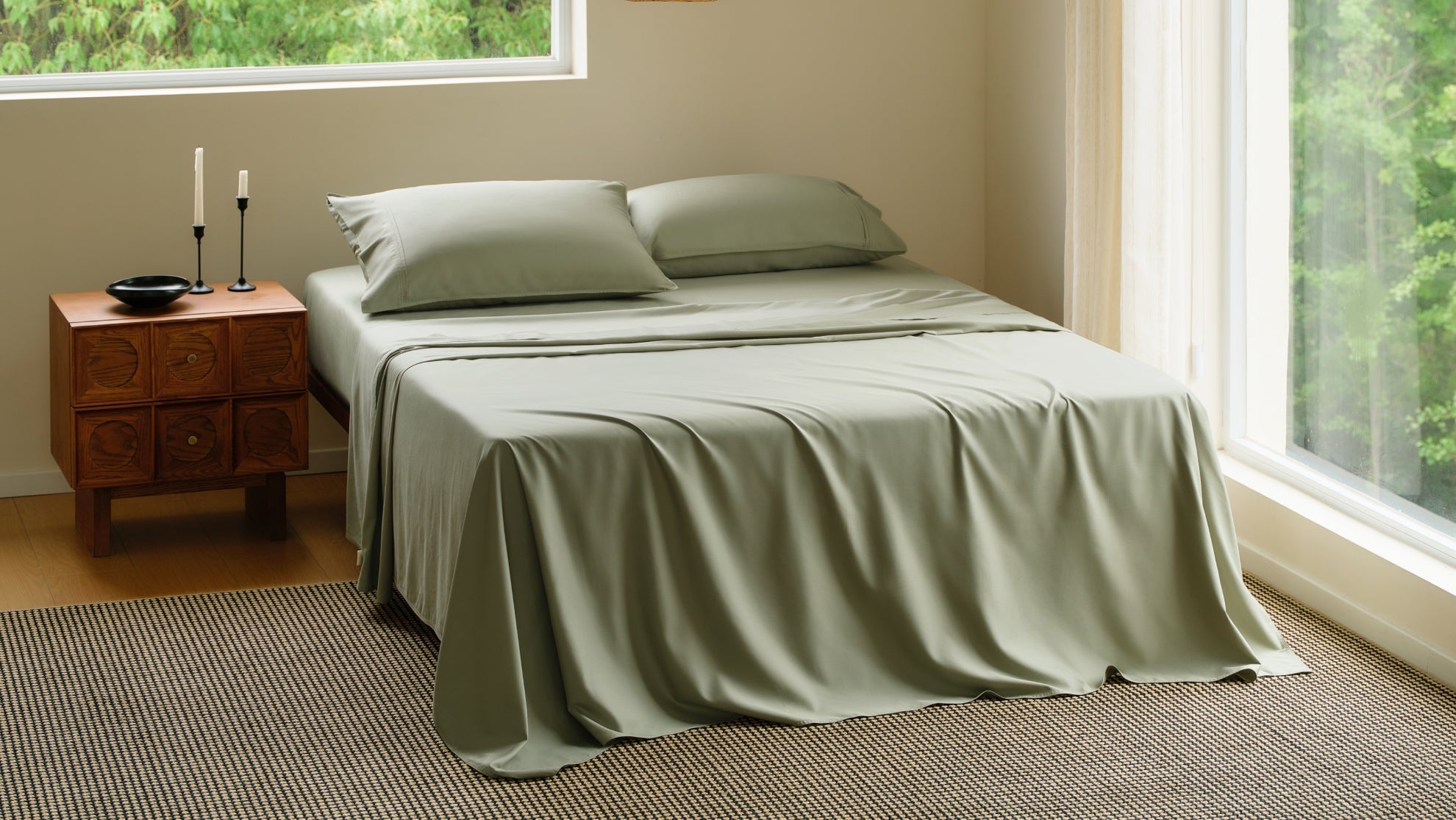 Minimalist bedroom featuring sage green bamboo cooling sheets on a neatly made bed near a large scenic window.