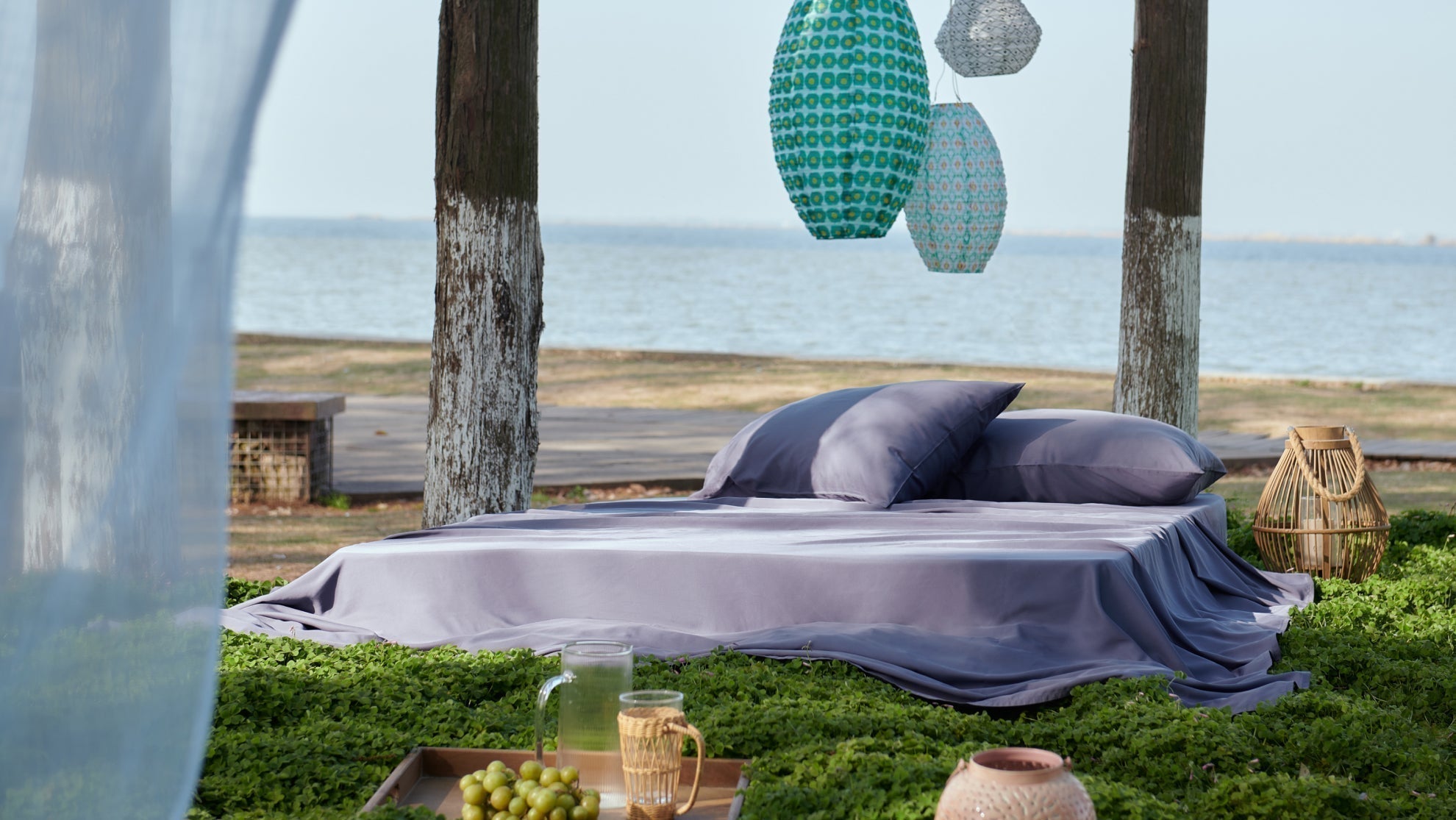 Purple 100% Cotton Sheets arranged on an outdoor bed near a scenic coastline at dusk.