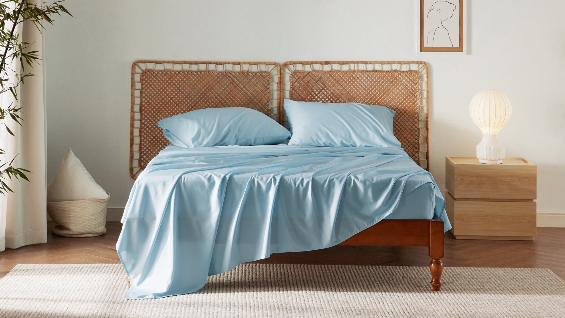 Light blue bamboo sheet set on a wooden bed with a woven headboard in a bright bedroom.