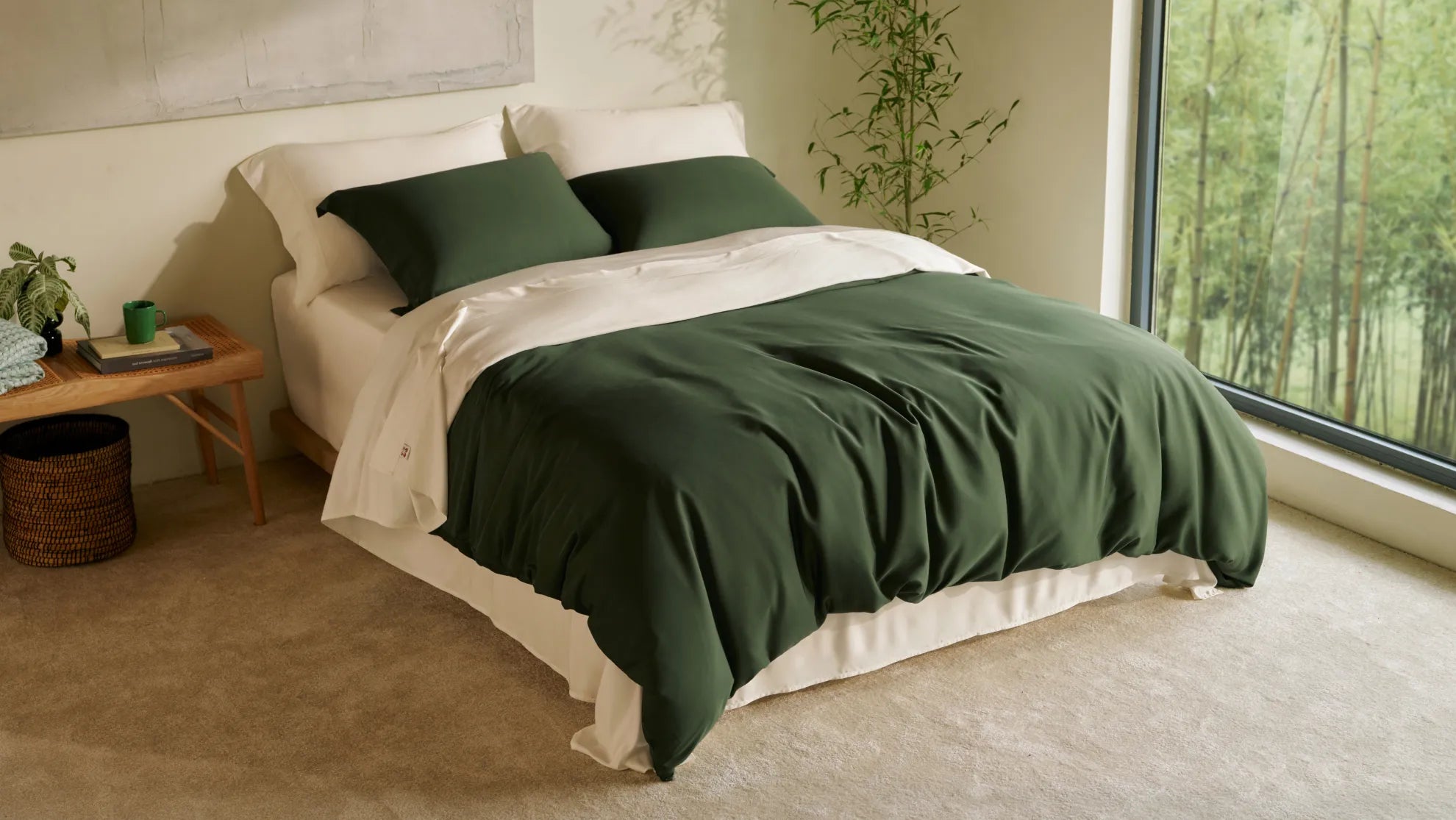 Green bamboo bedding set with white sheets in a bright bedroom beside a large window overlooking bamboo plants, showing a soft, breathable sleep setup.
