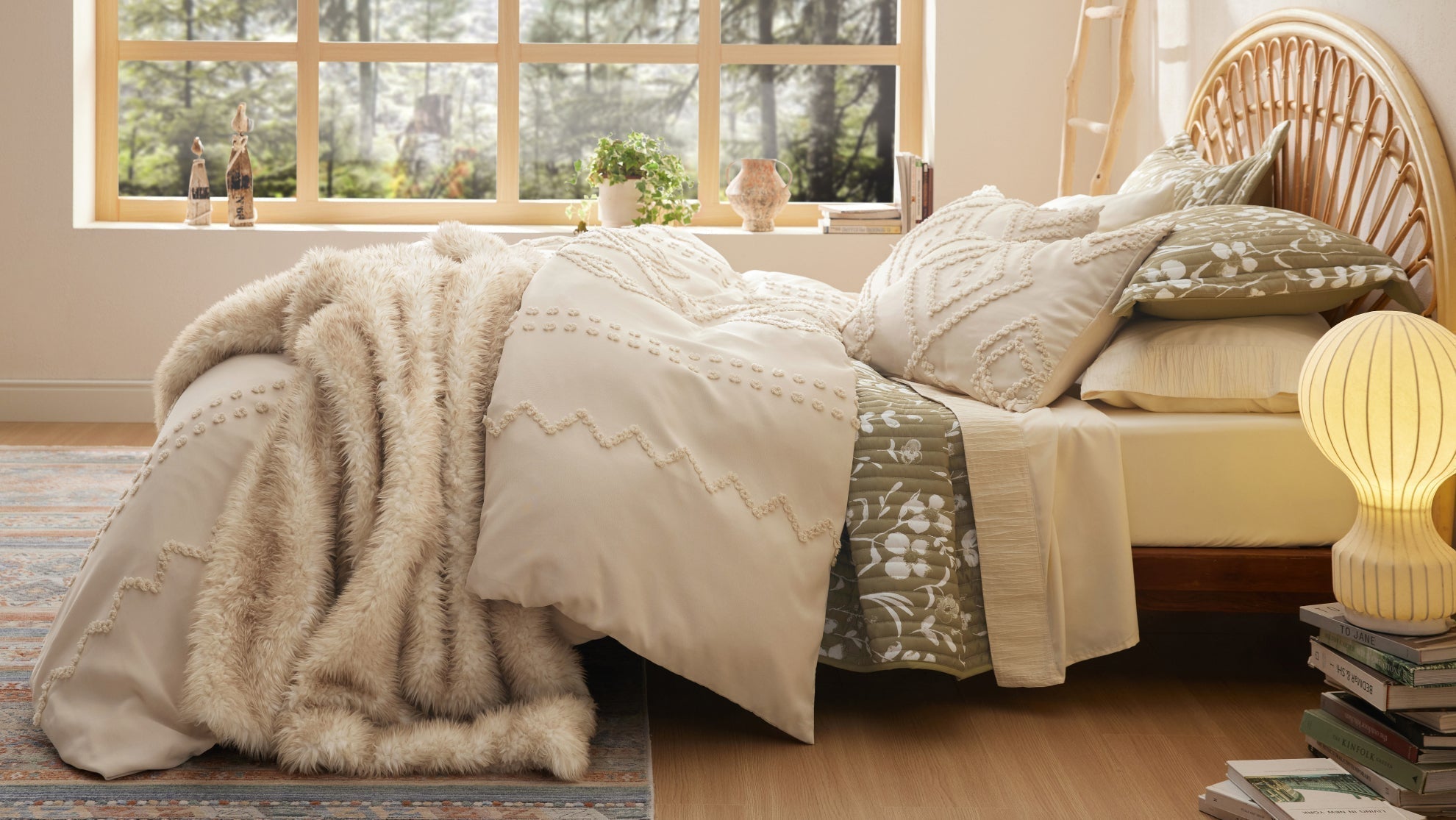 Layered bedding with a faux fur throw and green quilt on a rattan bed near a warm bedside lamp.