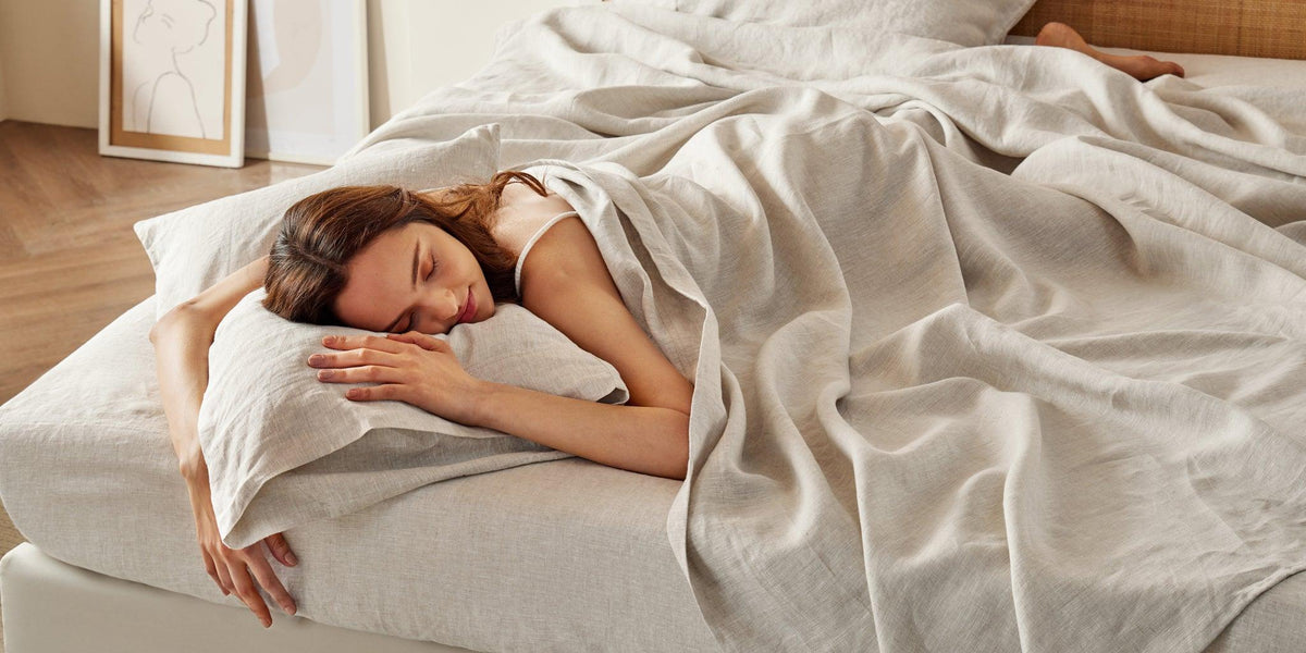 Woman sleeping peacefully on soft white linen cotton blend bedding in natural sunlit bedroom setting