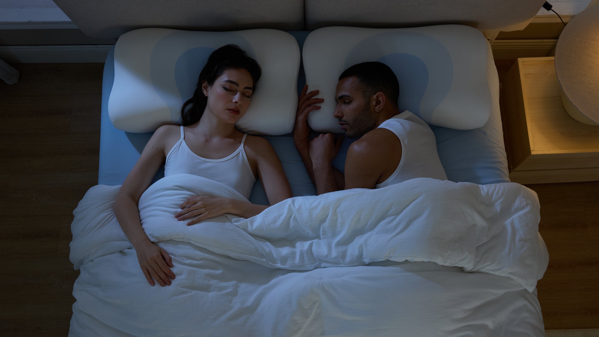 A couple sleeps peacefully on their backs using contoured pillows that ensure proper spinal alignment and restful sleep.