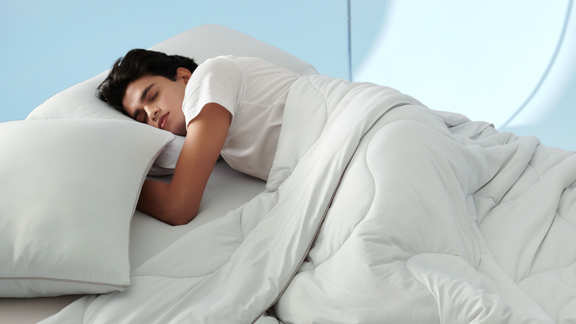 Person sleeping on white pillows under a lightweight white comforter in a cool blue bedroom.