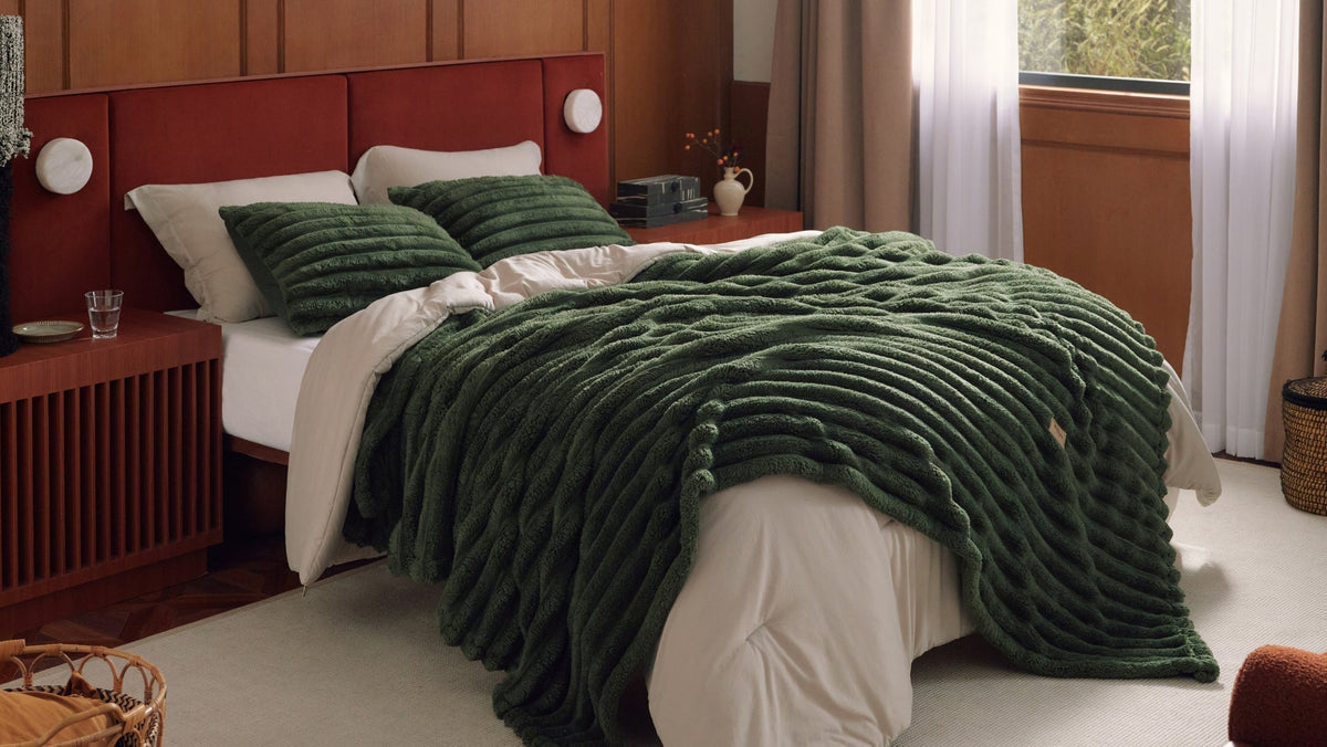 Bed with dark green textured throw and pillows, white bedding, wood nightstands, sheer curtains.
