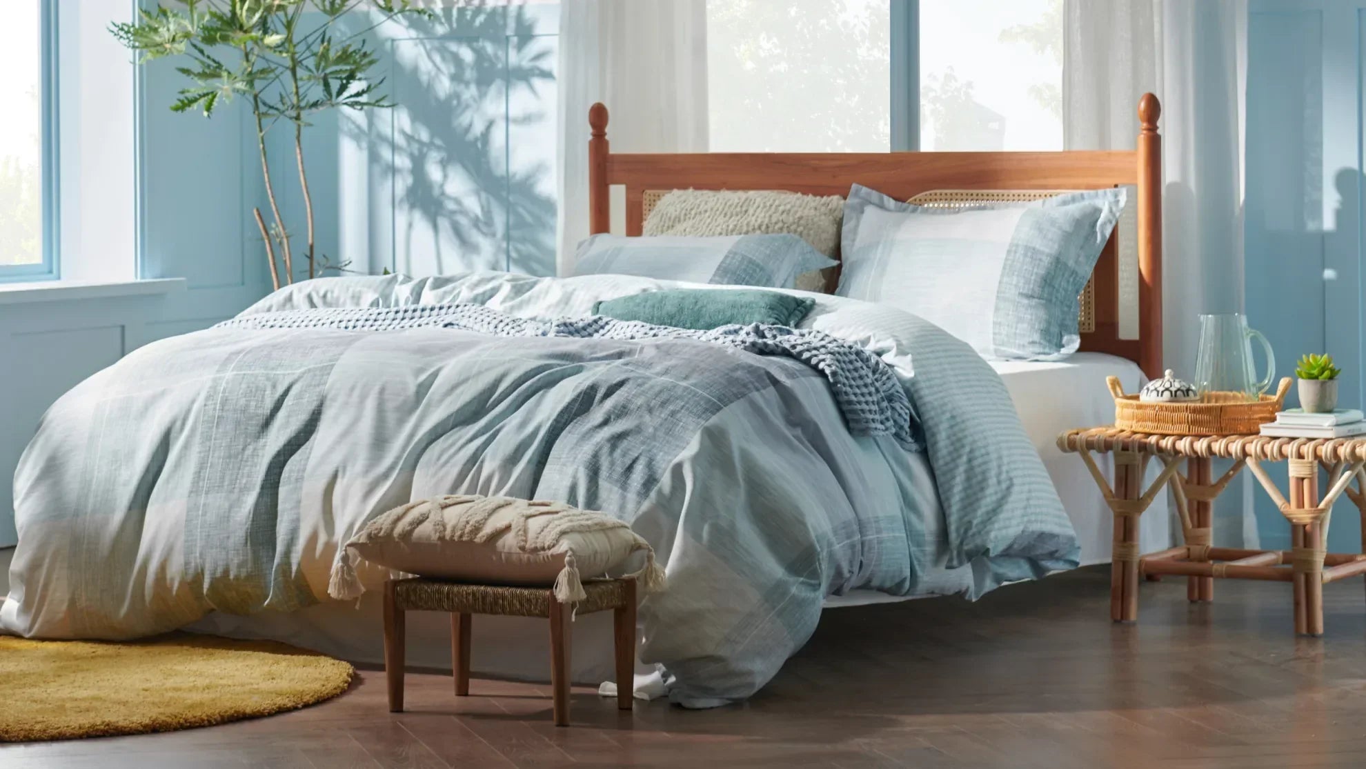 Sunlit bedroom with blue bedding, layered pillows, and natural wood furniture