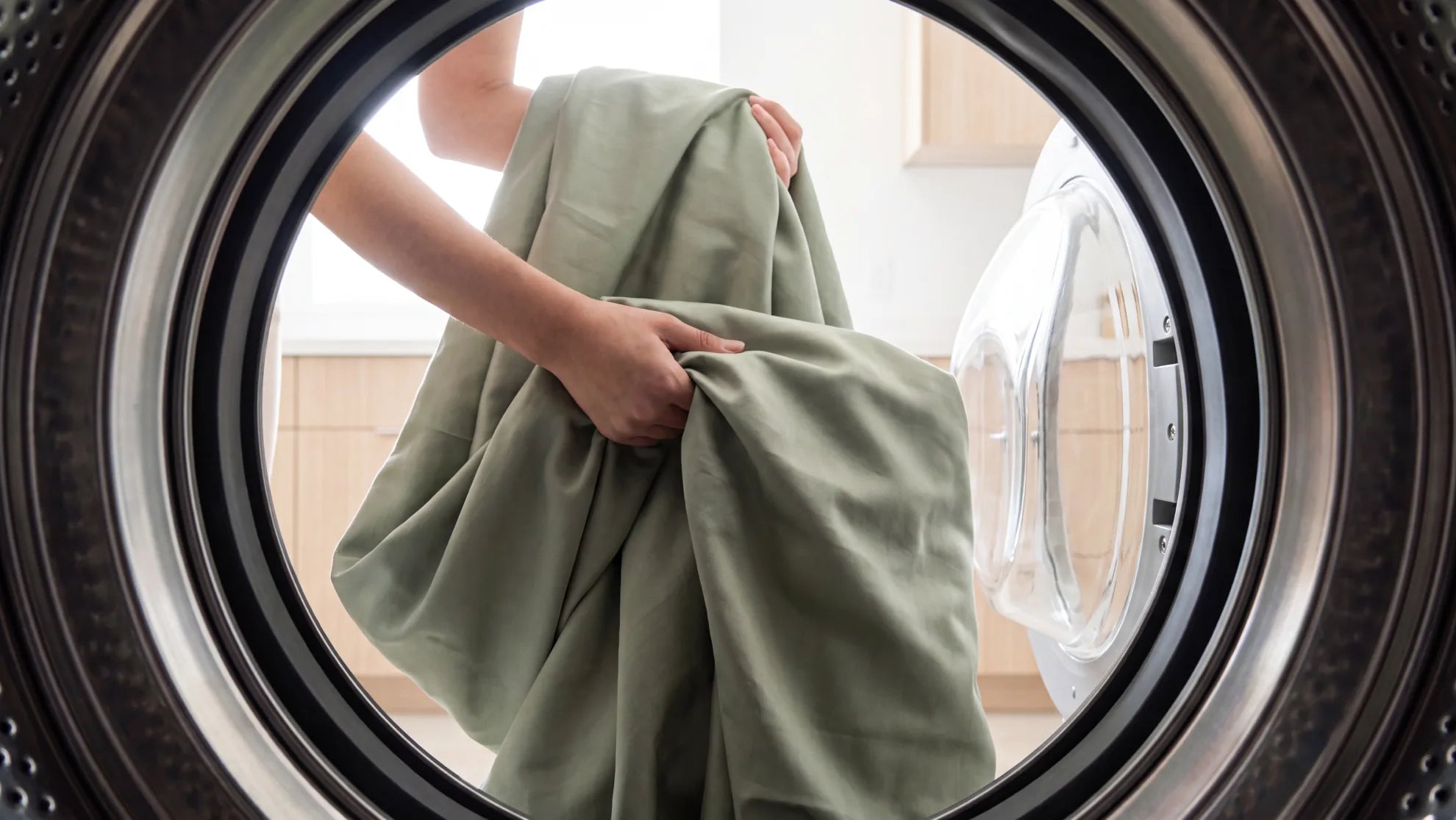 Green bed sheets being loaded into a front-loading washing machine