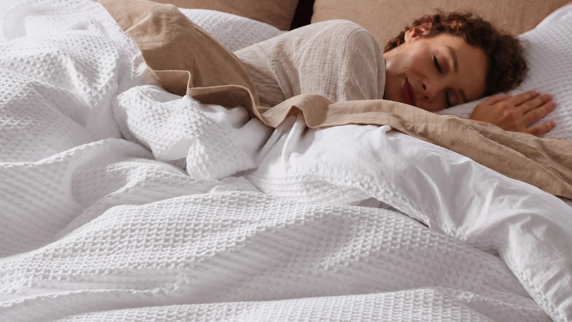 Woman sleeping under layered white bedding with a neutral top sheet