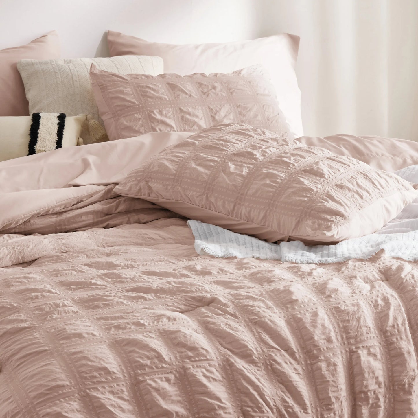 Blush pink seersucker plaid comforter set with textured pattern and decorative pillows.