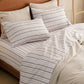 Cotton-Like white and dark striped sheet set with neutral pillowcases.