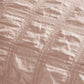 Close-up of light pink polyester seersucker fabric showing puckered plaid texture.