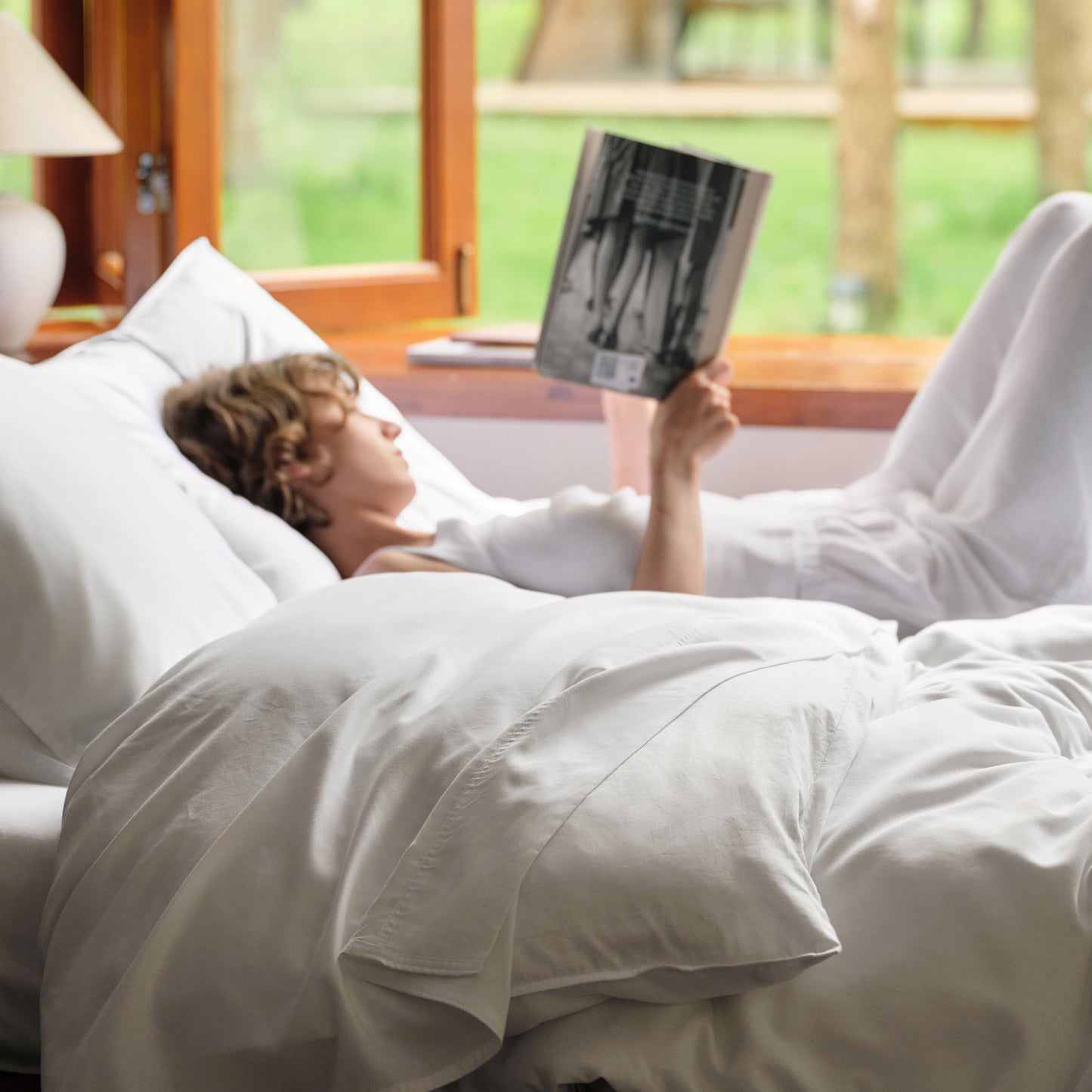 Person relaxing in bed, reading with soft white Serene Blend bamboo-cotton bedding.