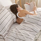 Cotton-like striped sheet set with dark pinstripes, woman reading in bed.