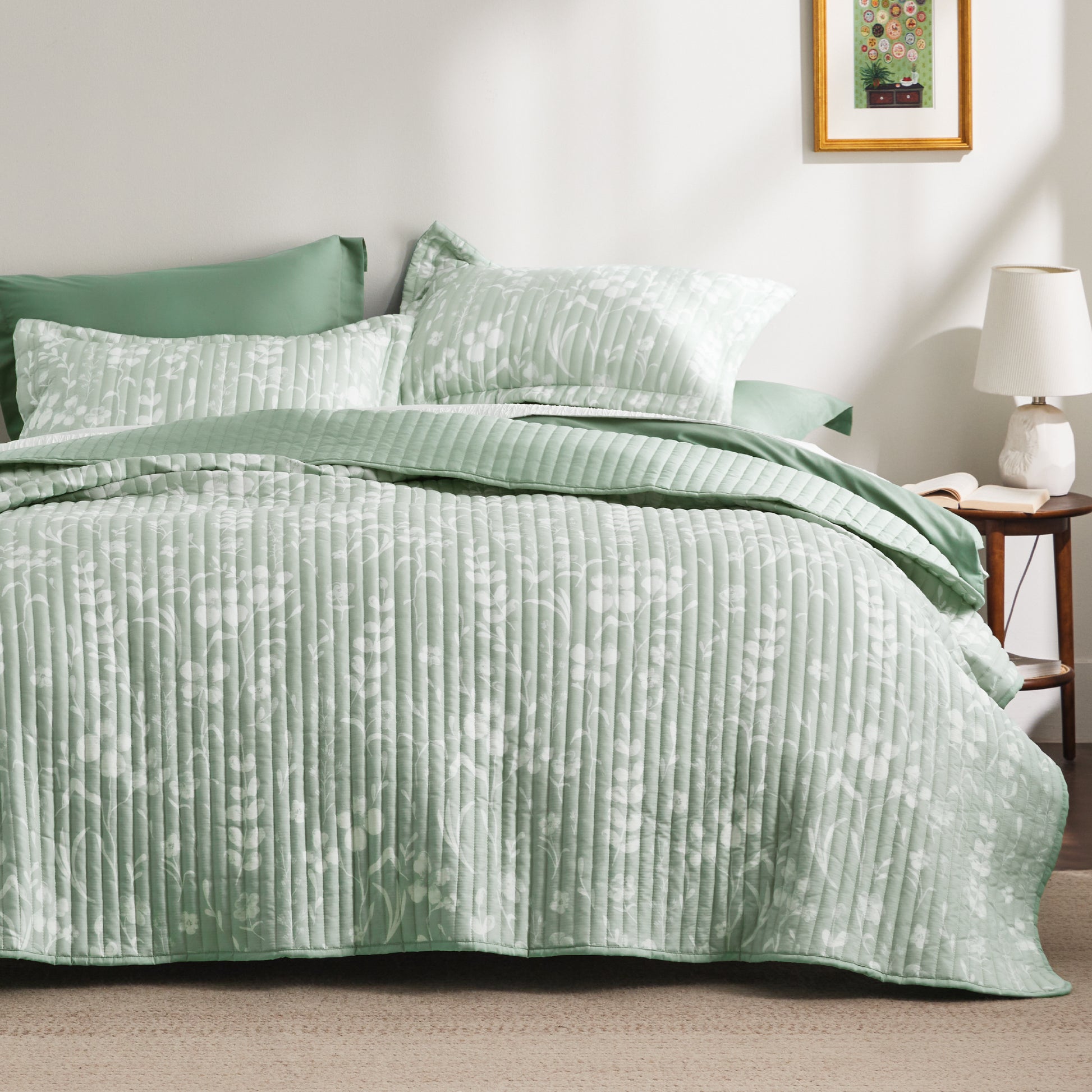 Soft green botanical quilt set with white floral pattern, vertical stitching, and matching shams.