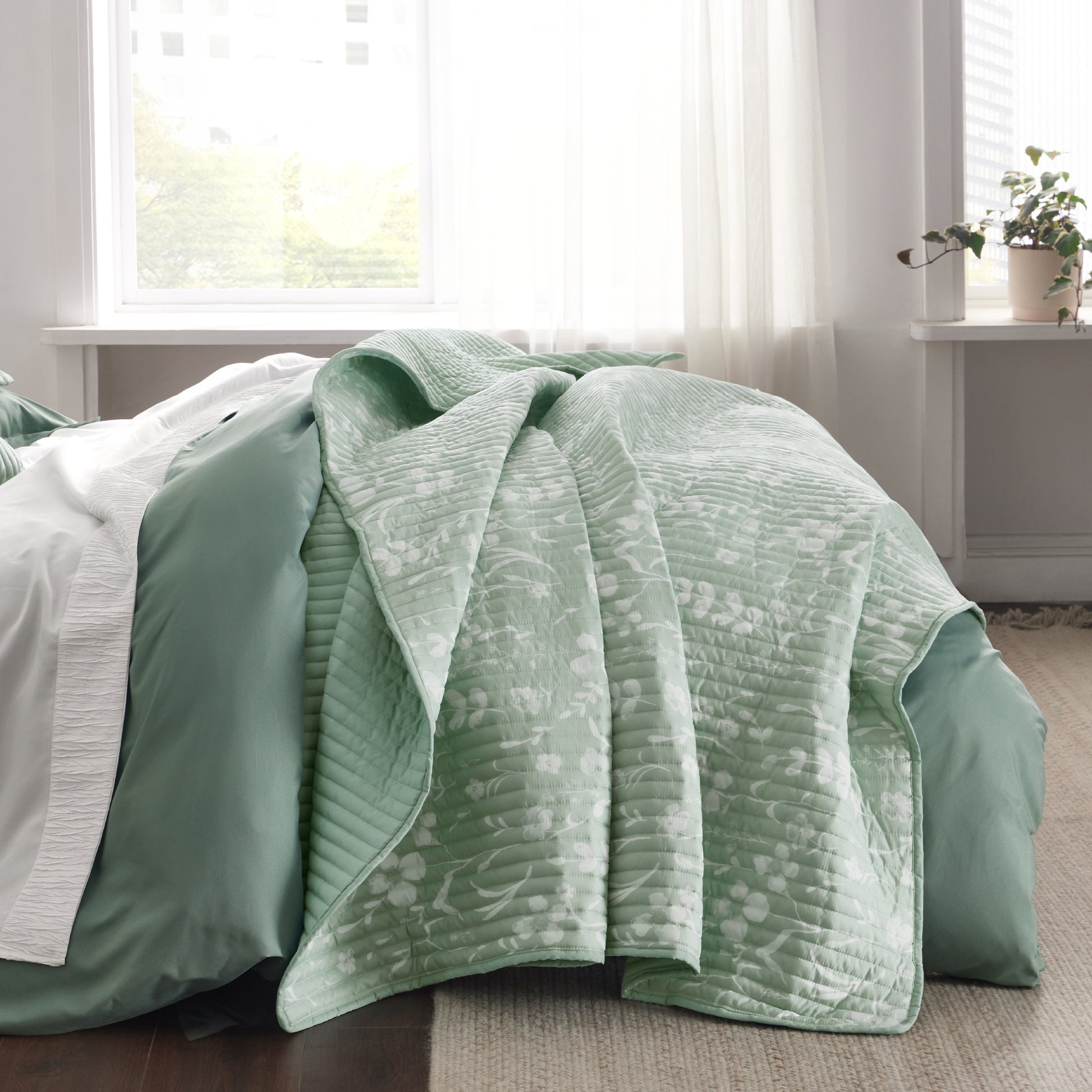 Botanical Quilt Set: Light green quilt with white floral pattern on bed.