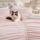 Pink ruched comforter set with bow detailing, featuring a fluffy cat on a tufted headboard.