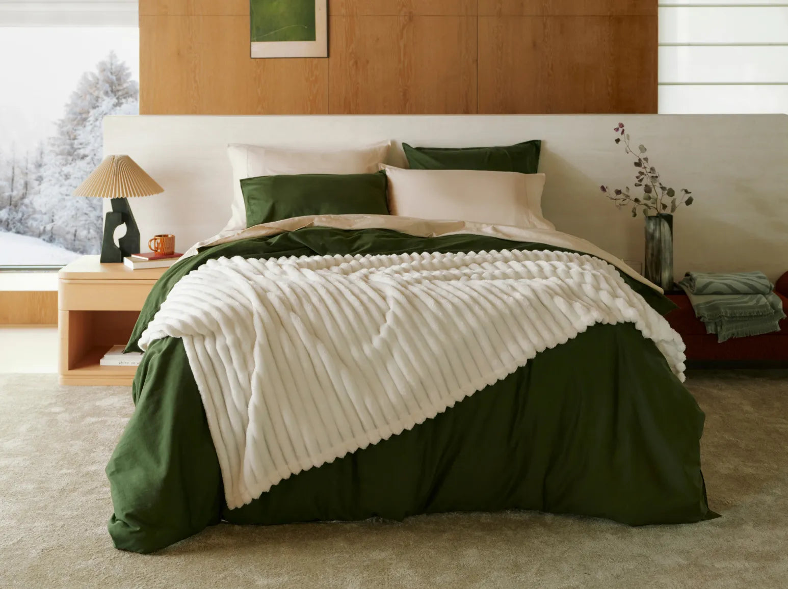 Bedroom with green bedding and white blanket, wooden headboard, and side table. 