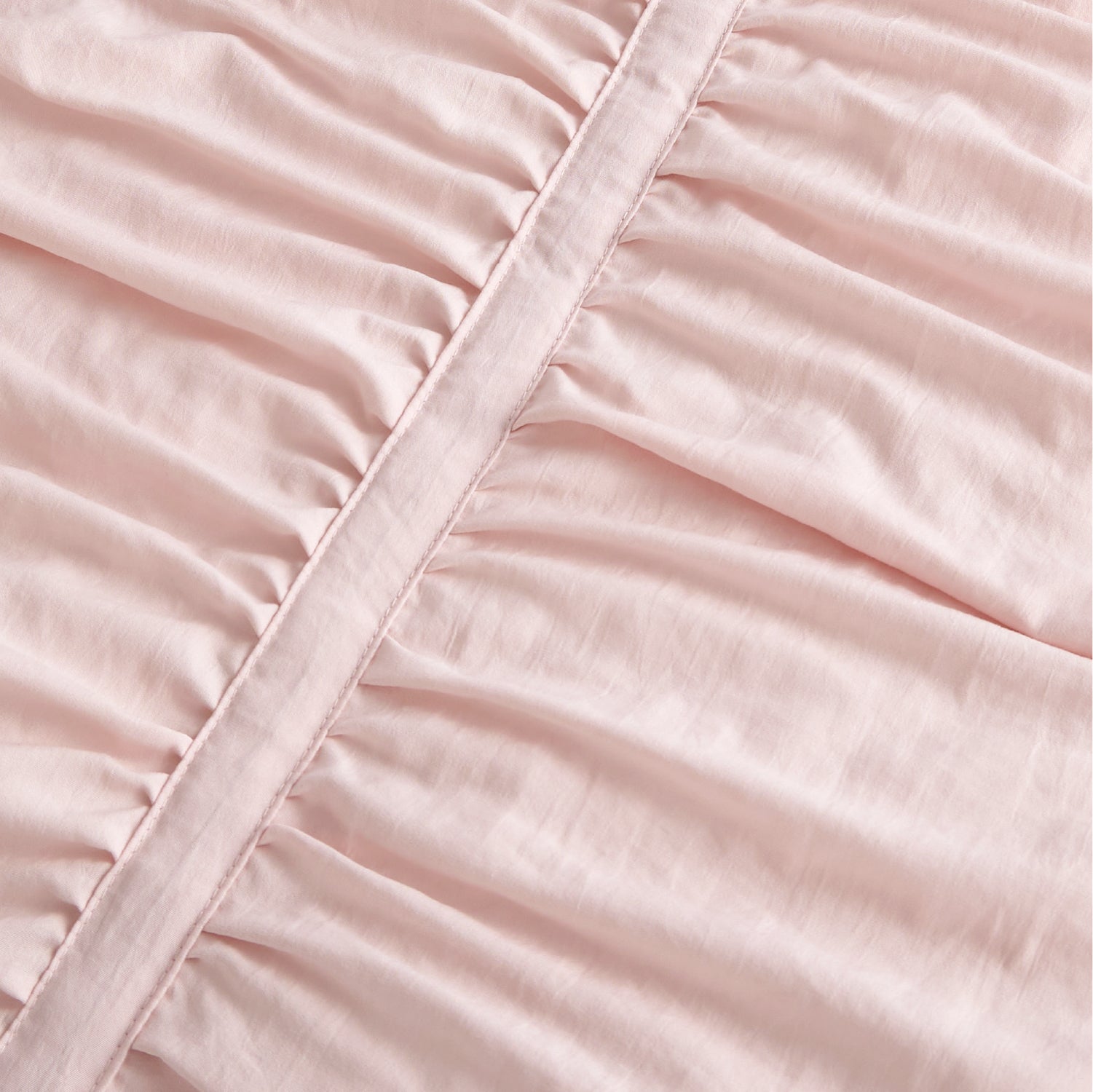 Pink polyester comforter close-up showing ruched fabric texture and decorative seam.