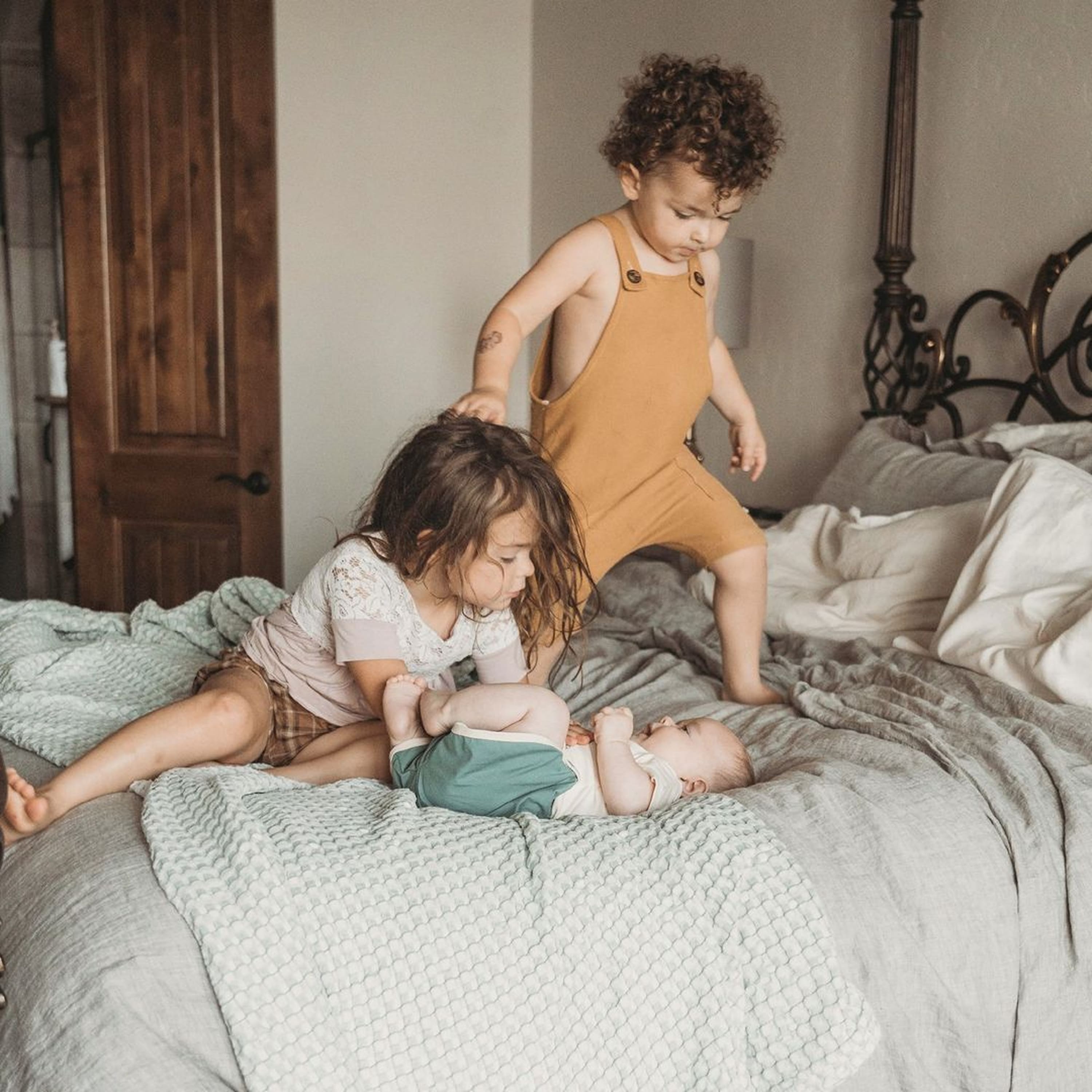Three children playing on a bed in a bedroom setting.
                                    